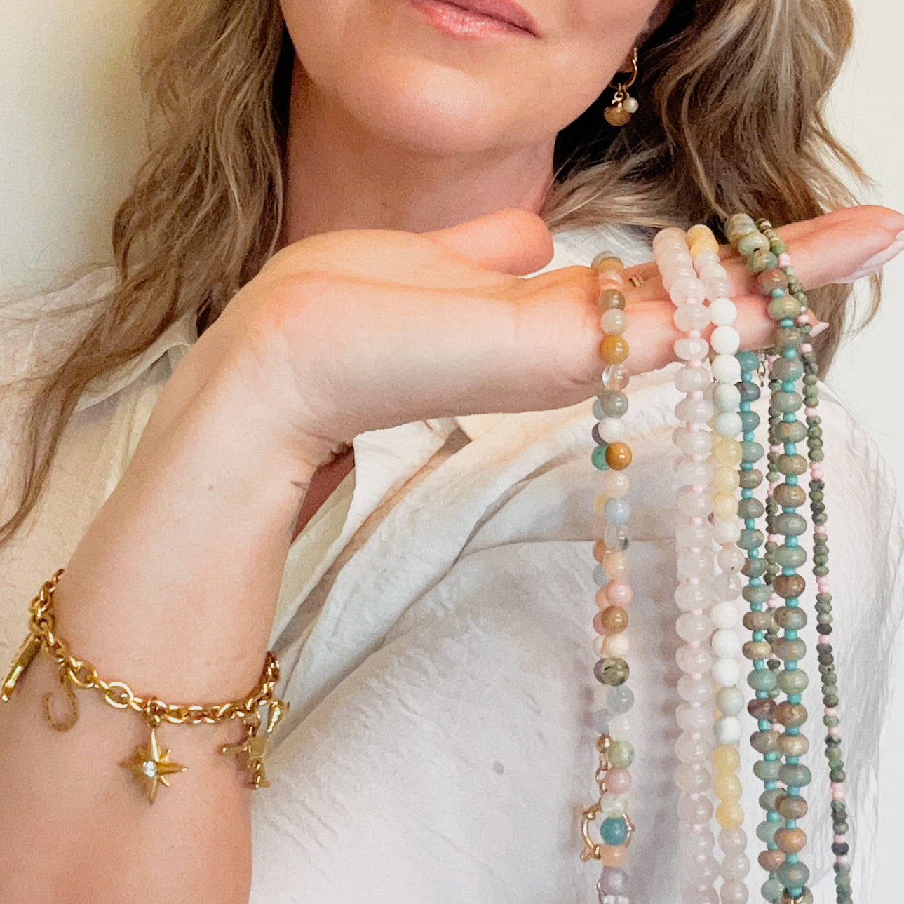 Woman holding multiple beachy  beaded necklaces with a gold charm bracelet o