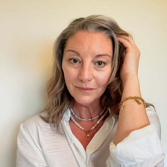 woman wearing beach inspired shell necklaces and golden western charm bracelet, meaningful jewelry that gives back to mental health awareness