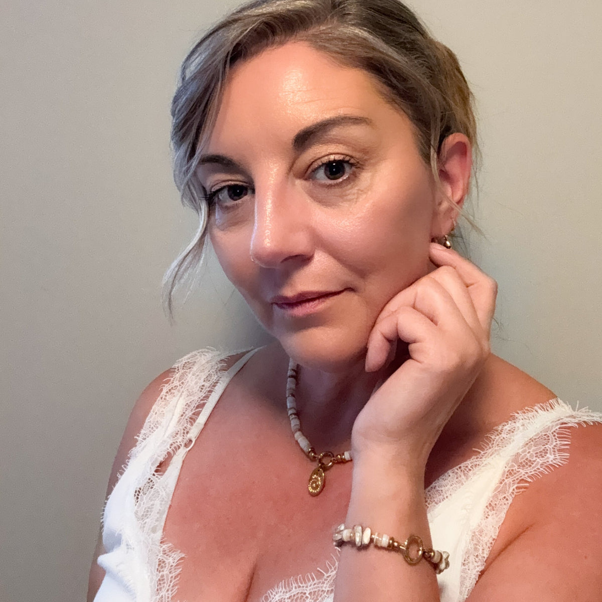 Woman wearing the Sunday Shell Necklace and matching bracelet with creamy shell beads, gold accents and shell charm